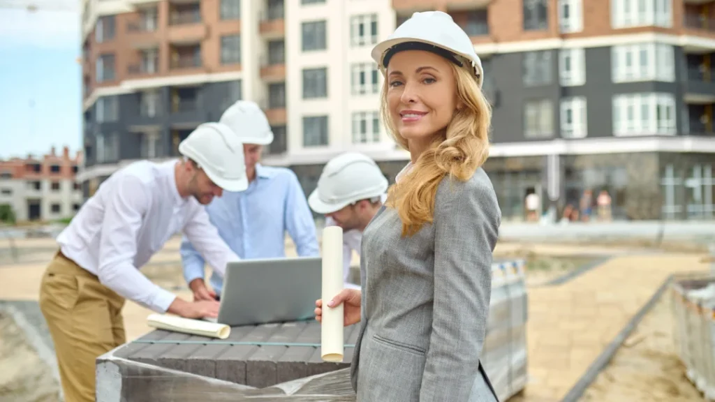 A woman in a hard hat and suit stands confidently before construction workers at a building expansion site in Quebec.