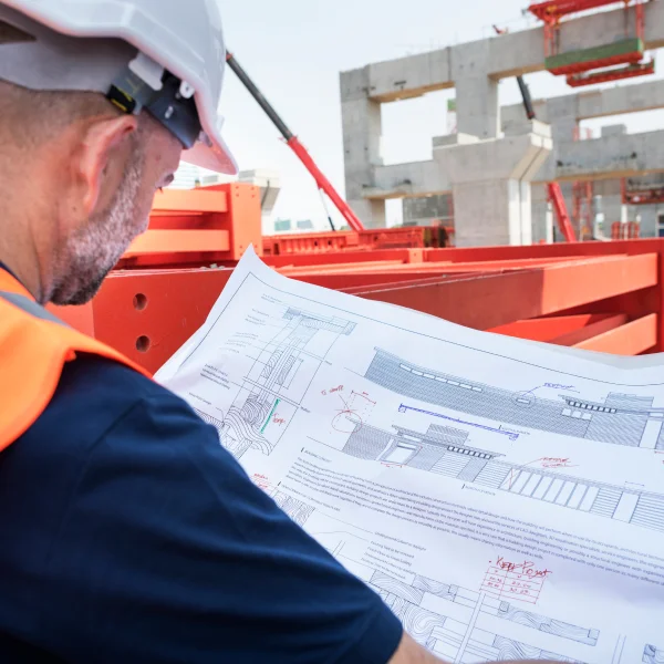 A man in a hard hat and safety vest examines a blueprint for a building expansion project in Quebec.