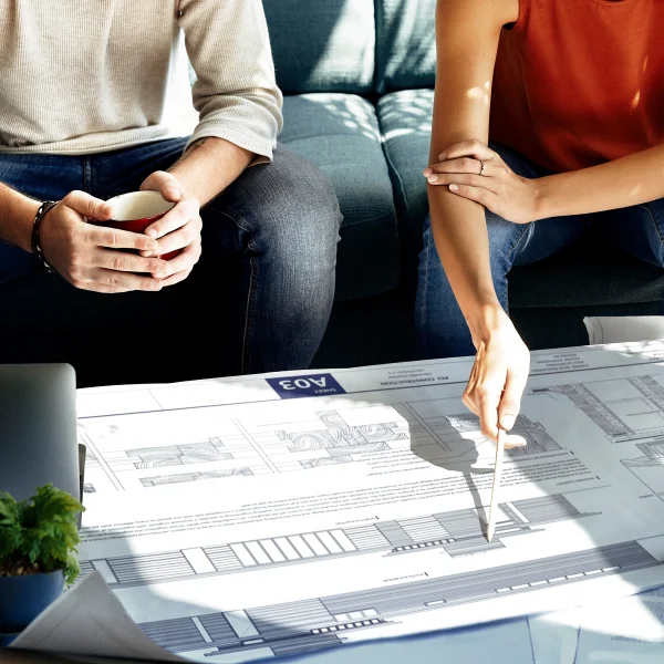 A man and woman review blueprints on a couch, discussing a building expansion project in Quebec.