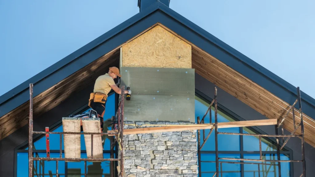 A man works on a house facade transformation using scaffolding for support and access to higher areas.