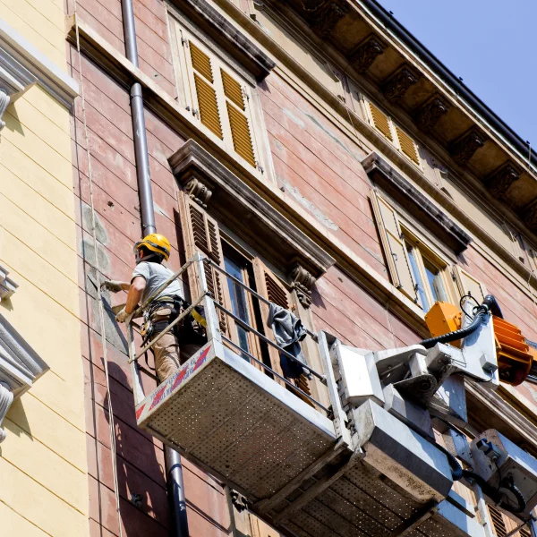 A man on a ladder working on a building's facade, part of a home transformation project.