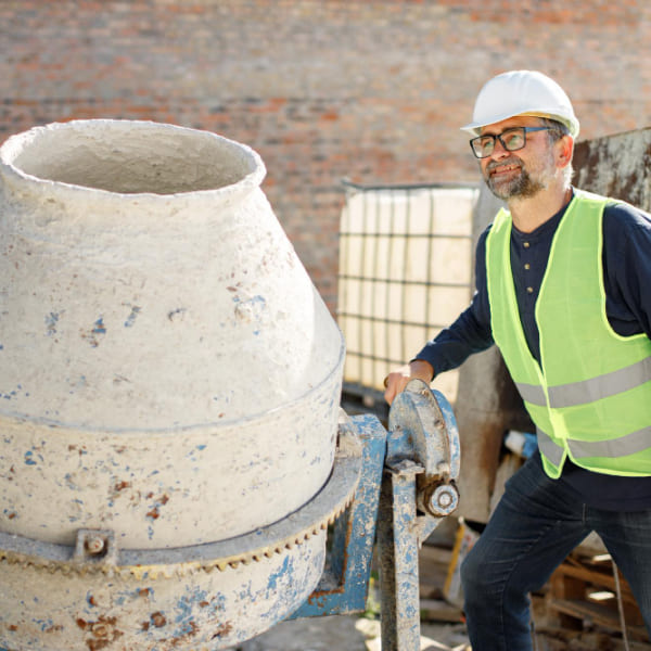Concrete contractor in hard hat and safety vest operating a cement mixer on a construction site