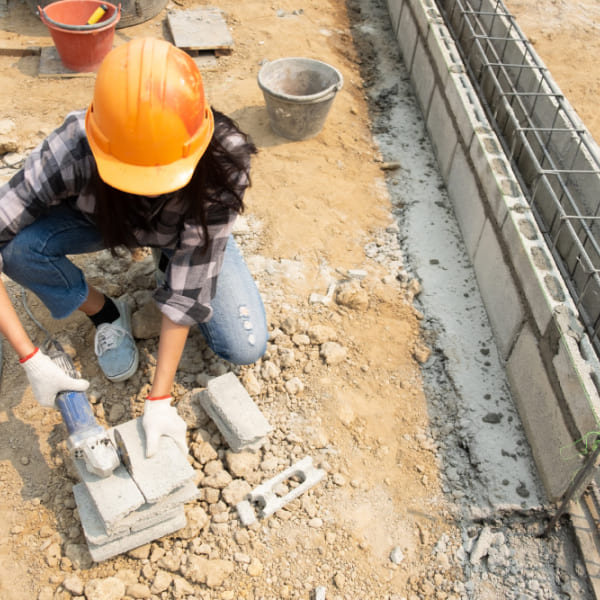 Female worker in hard hat cutting concrete blocks on a construction site, illustrating common mistakes to avoid in a concrete project